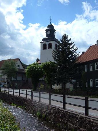 Die evangelische Kirche. An der Straße fließt die Laucha durch den Ort.